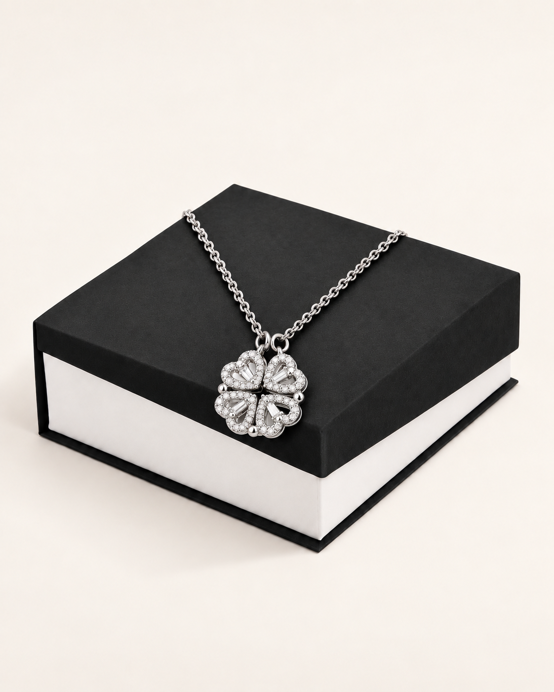 Silver-tone magnetic hearts necklace closed into a clover and displayed on a black gift box.