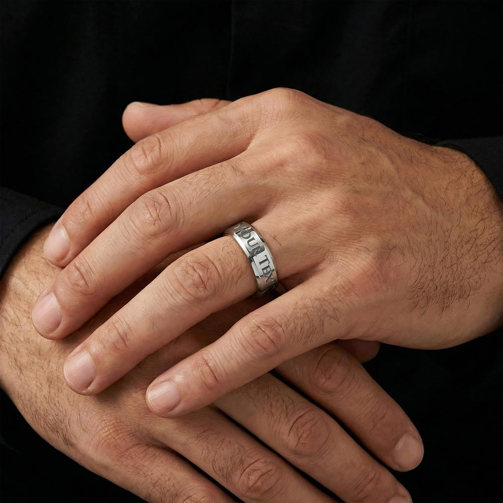 Close-up of a silver-tone men's engraved ring on a hand.