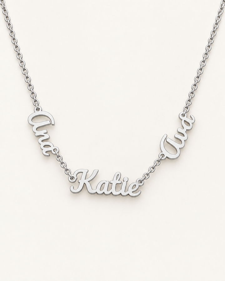 Silver-tone necklace with three connected script name pendants on an ivory background.