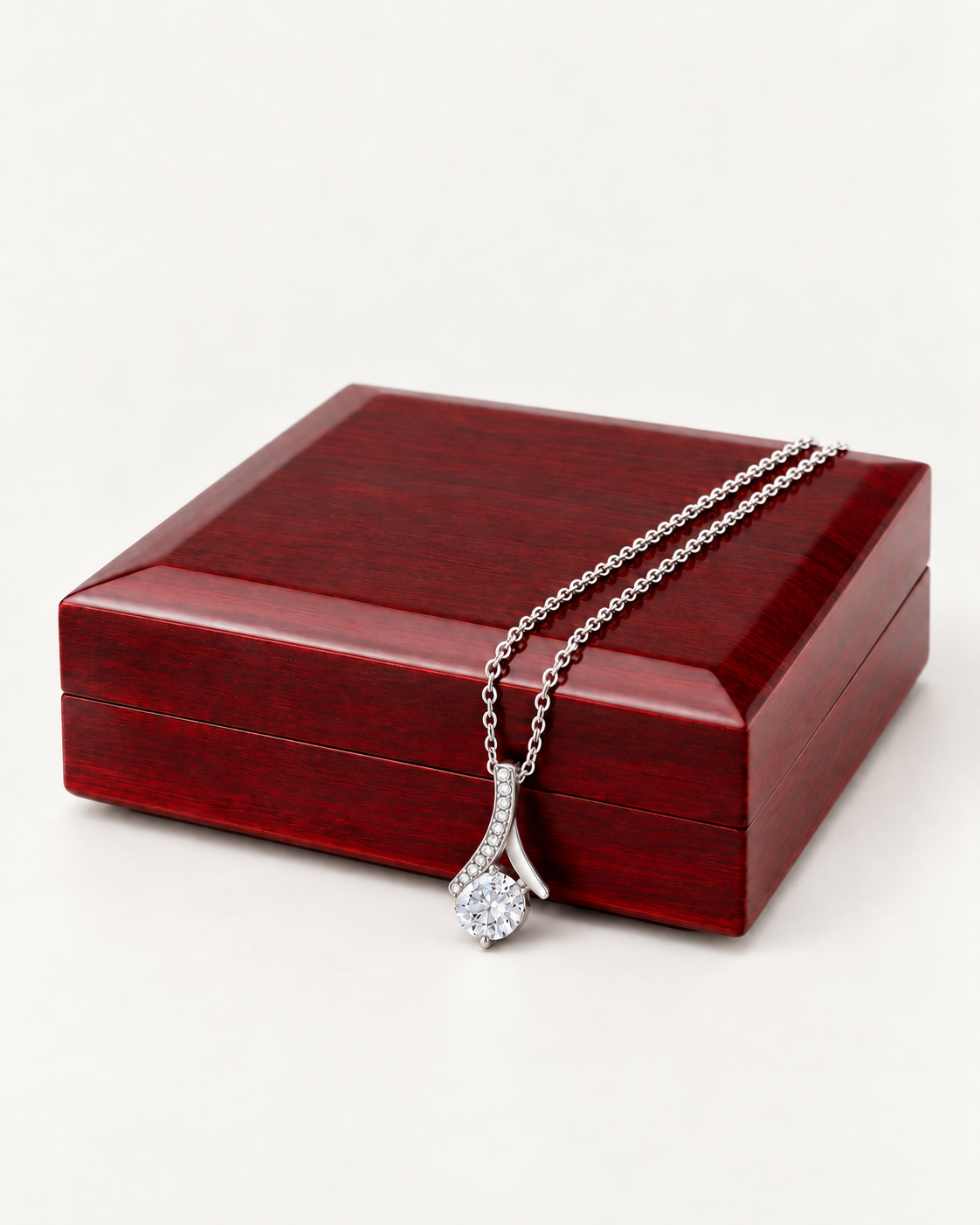 Silver-tone ribbon CZ necklace draped across a wooden gift box.
