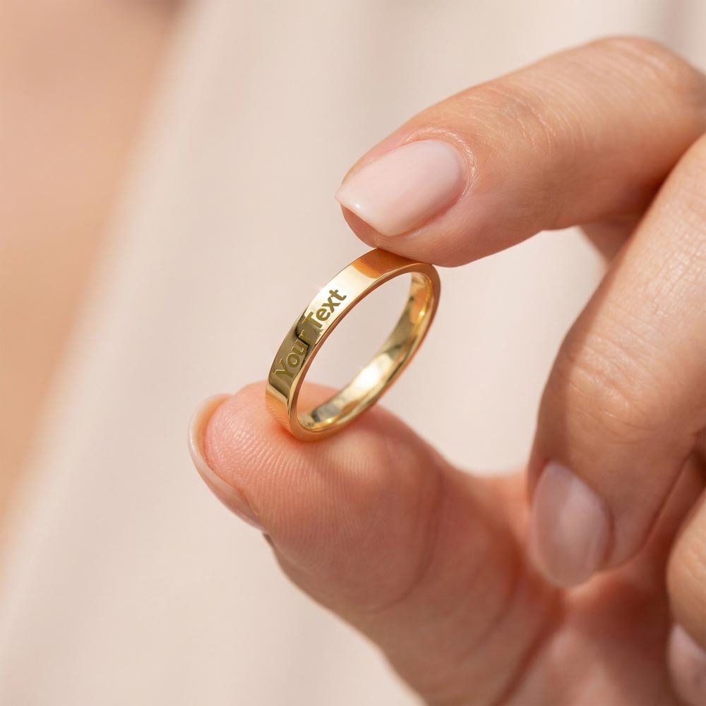 Slim gold-tone engraved ring held between fingertips to show its profile.