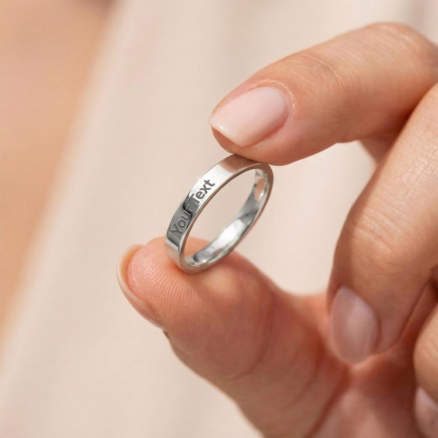 Slim silver-tone engraved ring held between fingertips to show its profile.