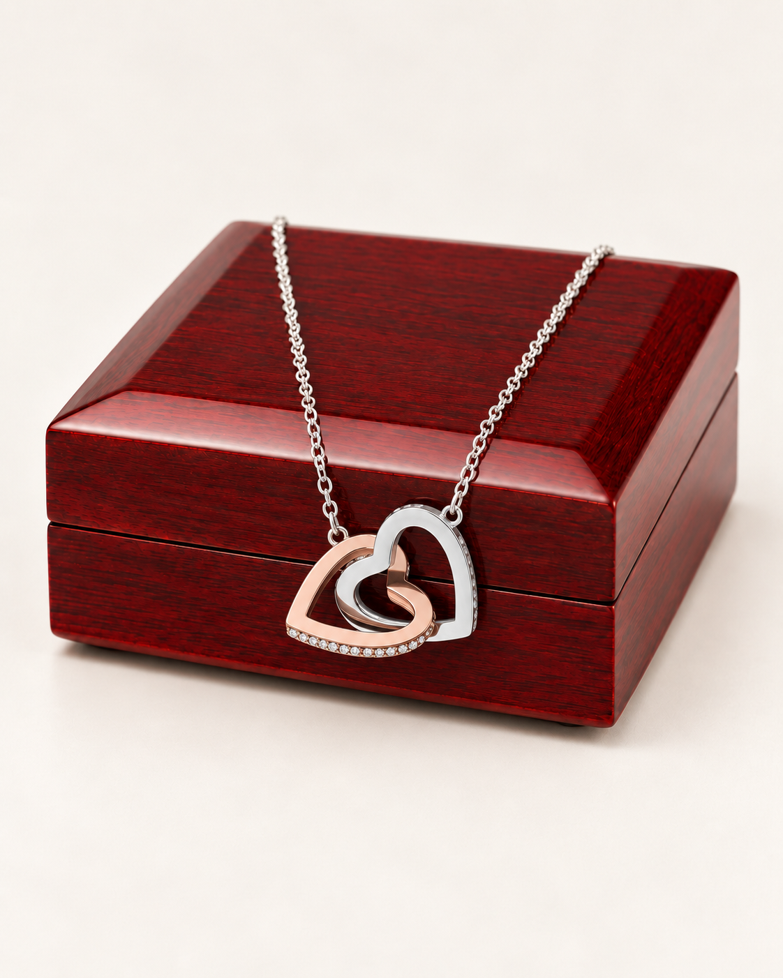 Two-tone interlocking hearts necklace draped across a wooden gift box.