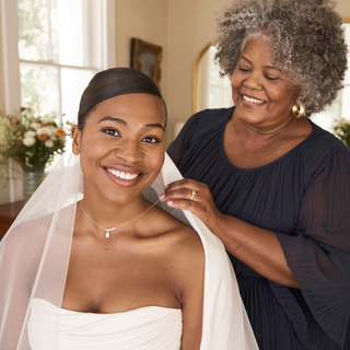 Bride smiling while a woman helps fasten her necklace.