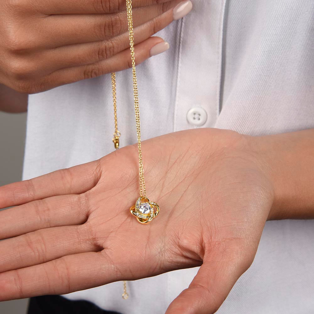 Woman holding a gold-tone Love Knot CZ pendant against her palm.