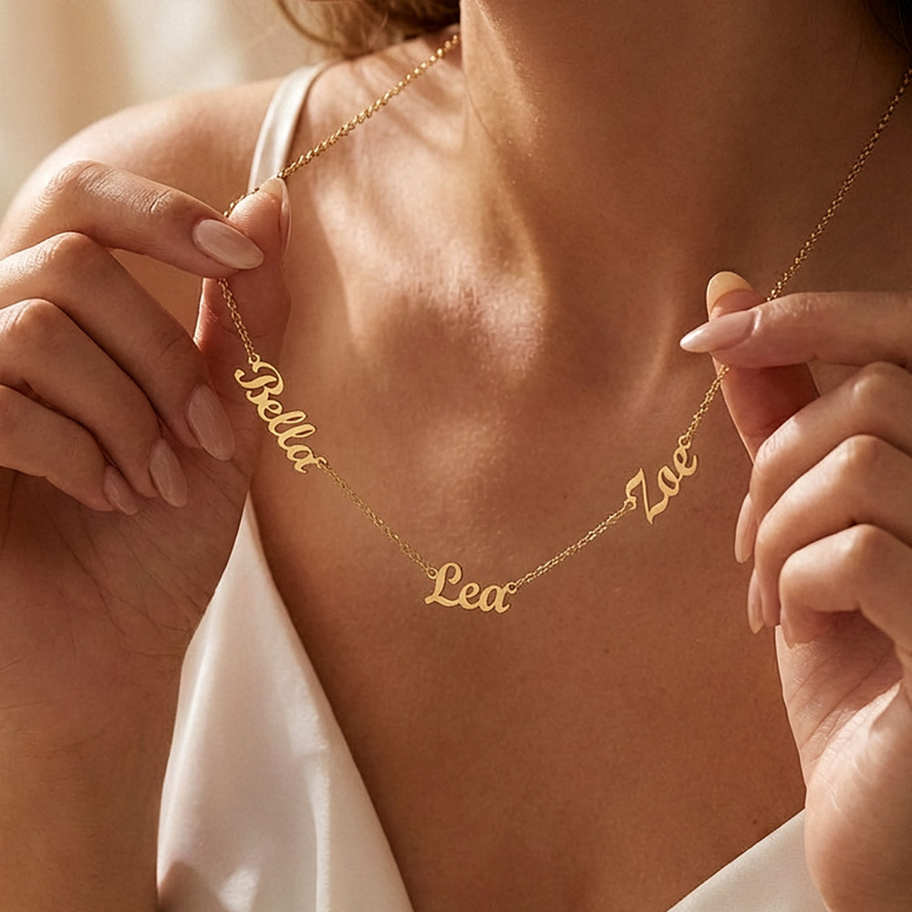 Woman holding a gold-tone three-name necklace across her neckline.