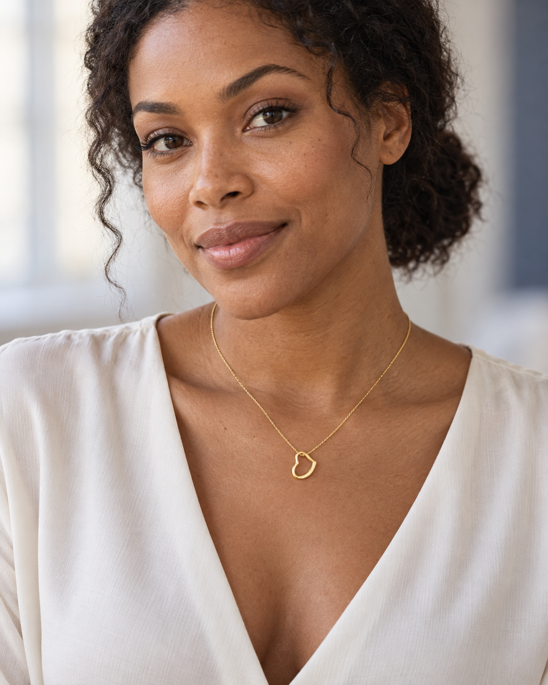 Woman wearing a delicate gold-finish open-heart necklace with an ivory blouse.