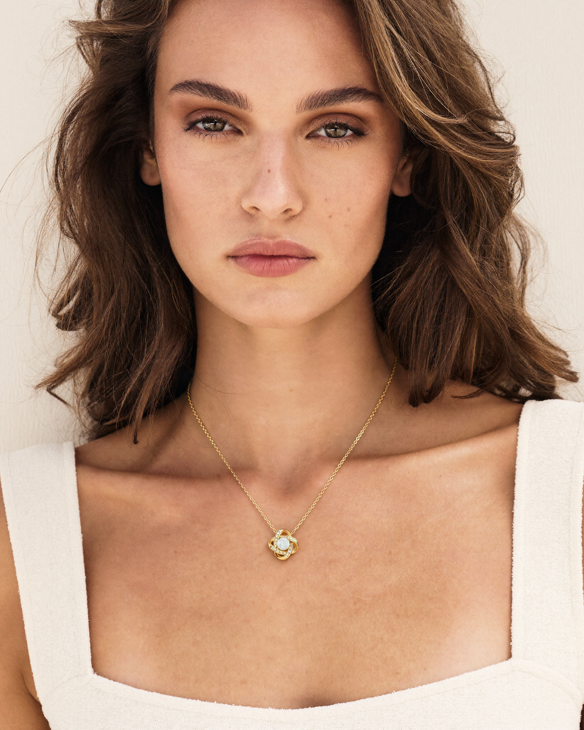 Woman wearing a gold-tone Love Knot necklace with an ivory square-neck top.