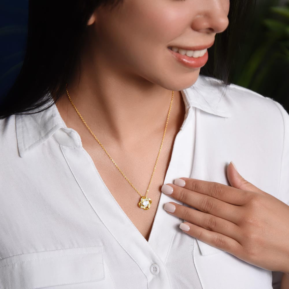 Woman wearing a gold-tone Love Knot pendant necklace with a white blouse.