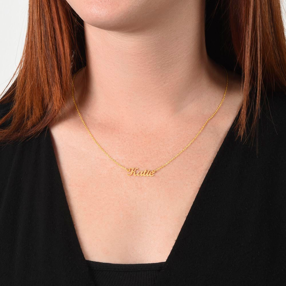 Woman wearing a gold-tone script name necklace with a black V-neck top.