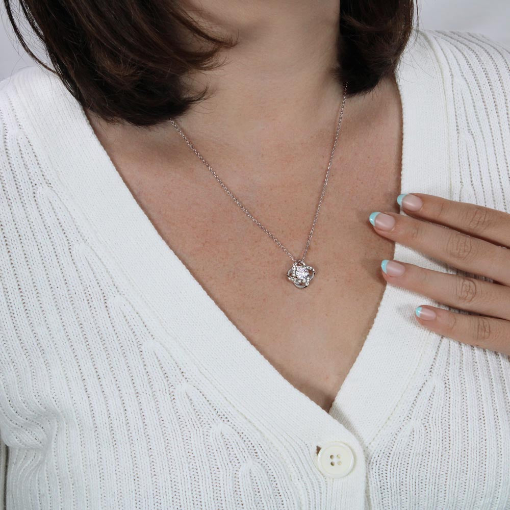 Woman wearing a silver-tone Love Knot pendant necklace with a white blouse.