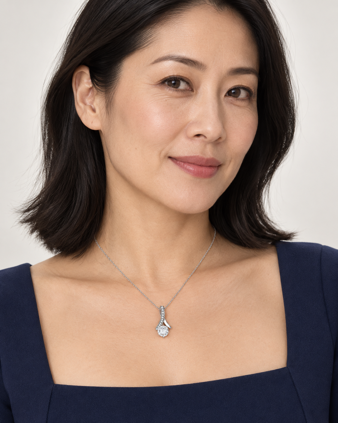 Woman wearing a silver-tone ribbon CZ necklace with a navy square-neck top.