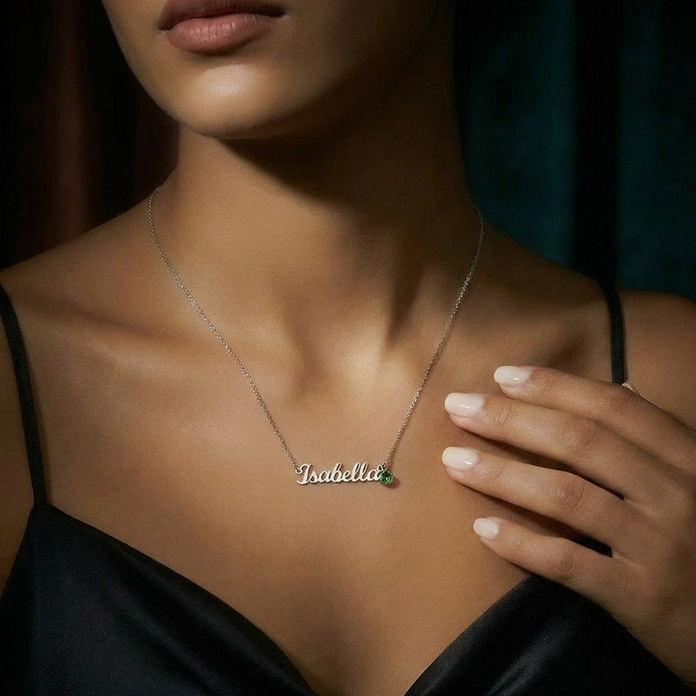 Woman wearing a silver-tone script name and birthstone necklace with a black satin top.