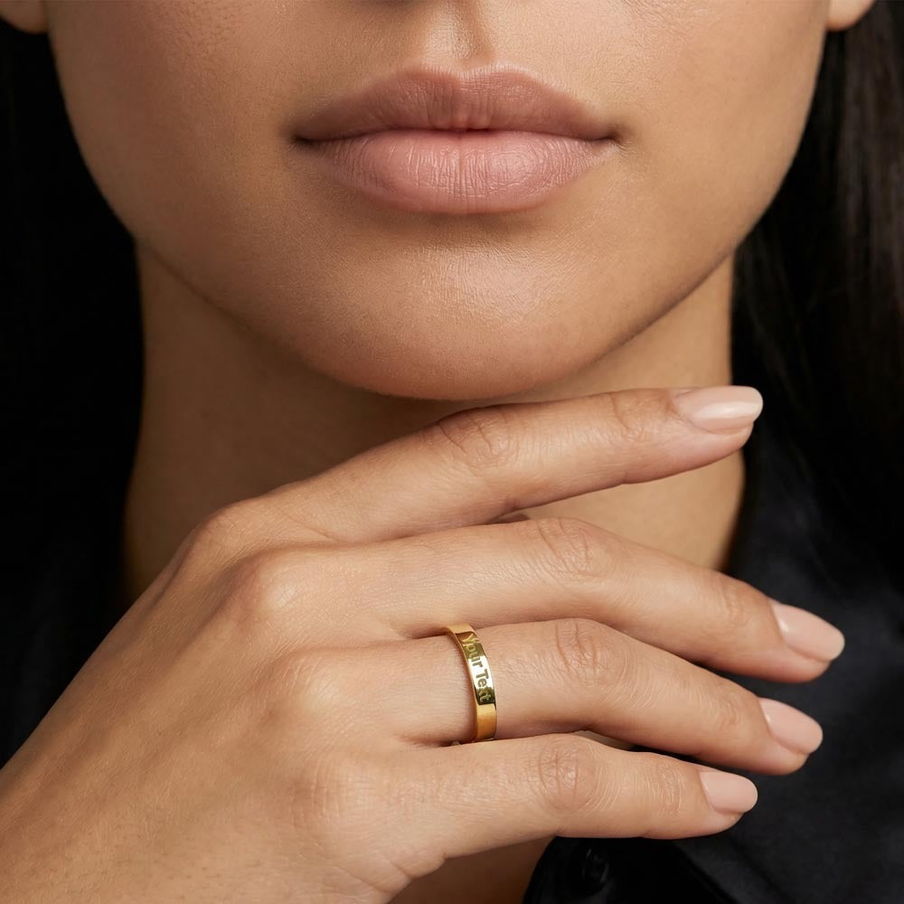Woman wearing a slim gold-tone engraved ring with her hand near her chin.